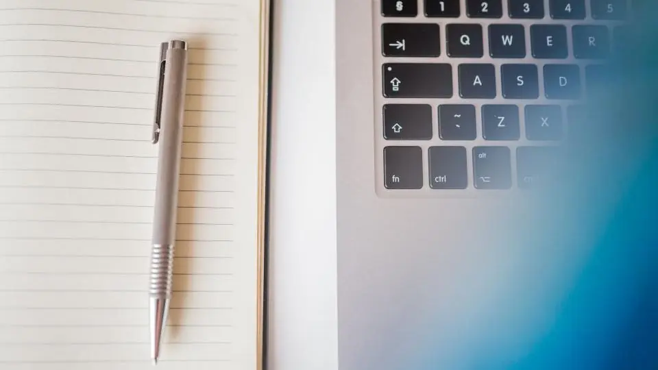 A notebook and pen beside a laptop