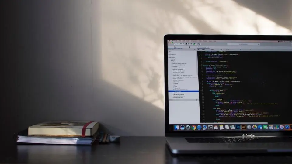 Code on a laptop screen beside a stack of books