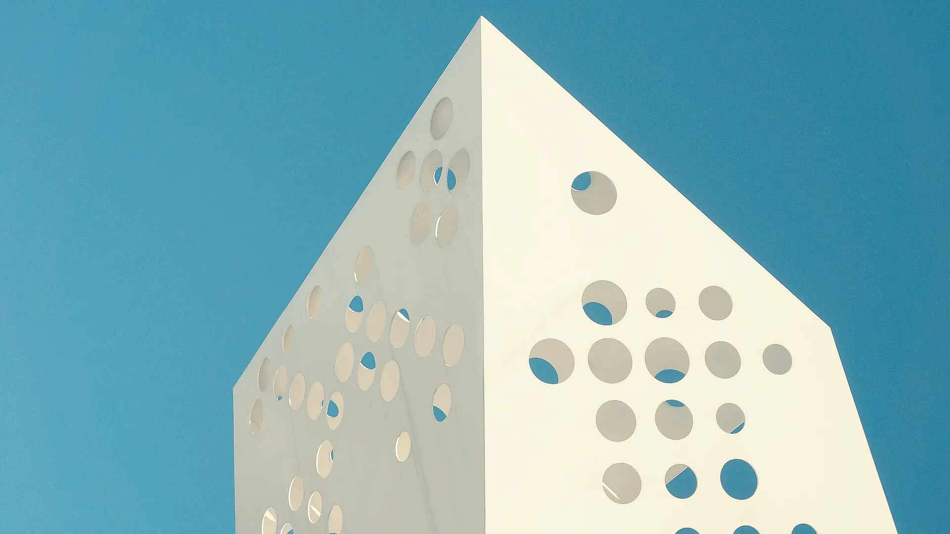 A white perforated building against a teal sky